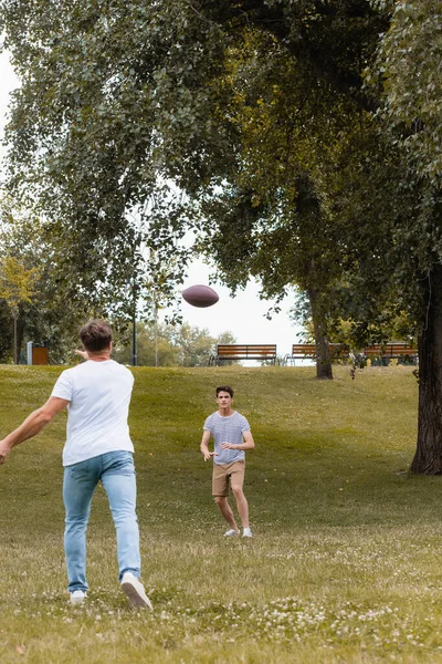 Back View Father Throwing Regby Ball Teenager Son Green Park — стоковое фото