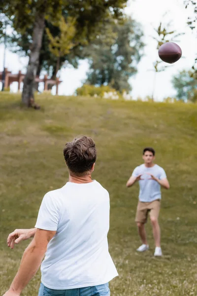 グリーンパークの10代の息子の近くにラグビーボールを投げる父親の選択的な焦点 — ストック写真