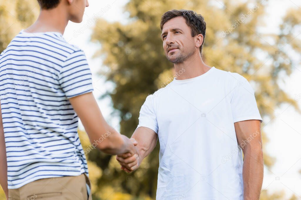 father and teenager son in t-shirts shaking hands in park 