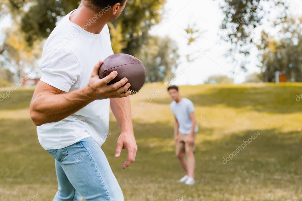 selective focus of man throwing rugby ball to son in park 