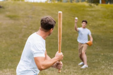 back view of father holding softball bat while playing baseball with teenager son  clipart