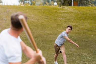 selective focus of teenager boy throwing ball while playing baseball with father clipart