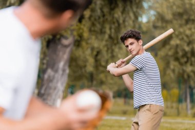 Beyzbol sopasıyla babasıyla parkta beyzbol oynayan konsantre genç bir çocuk.