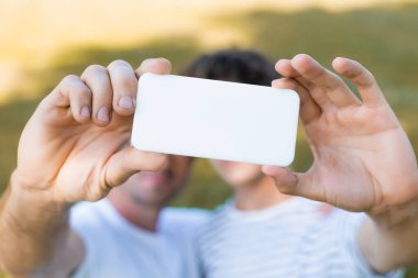 Akıllı telefonun seçici odak noktası baba ve ergen oğlunun selfie çekmesi. 
