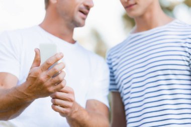 Ergen oğlunun yanında elinde akıllı telefon tutan bir adamın görüntüsü. 