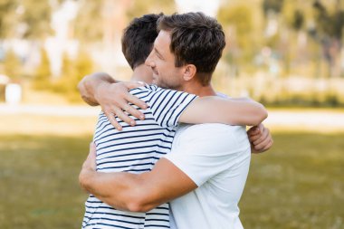side view of father and teenager son hugging outside clipart