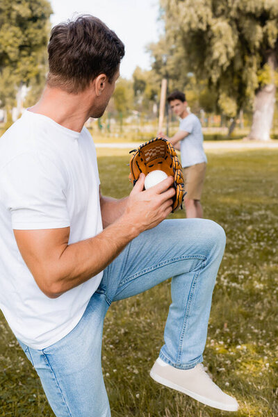 selective focus of man in leather glove posing while playing baseball with teenager son in park 