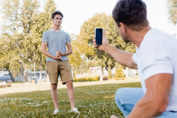 在公园里 当爸爸用智能手机拍照时 男孩摆出一副很有选择的姿势 — 图库照片
