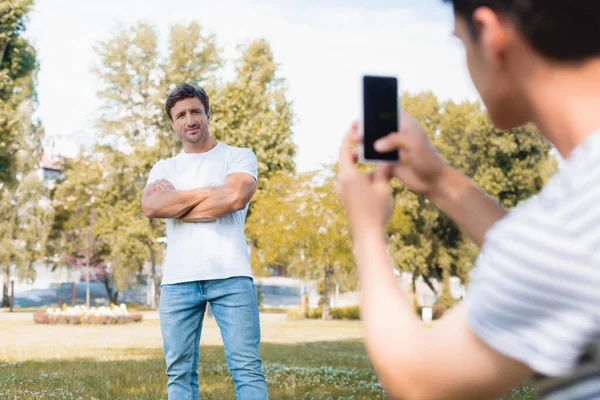 当少年男孩在公园拍照时 男人交叉双臂站立的选择性焦点 — 图库照片