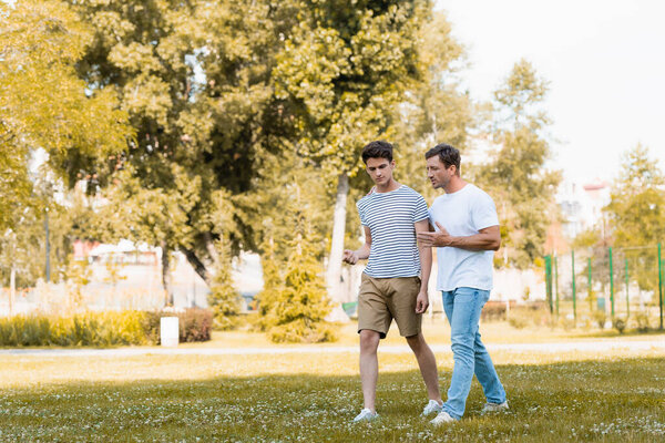 мужчина жестикулирует во время прогулки и разговора с сыном-подростком в парке 