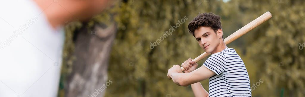 horizontal image of focused teenager boy with softball bat playing baseball with father in park
