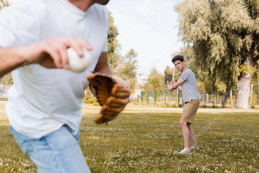 selective focus of teenager son with softball bat looking at father while playing baseball in park