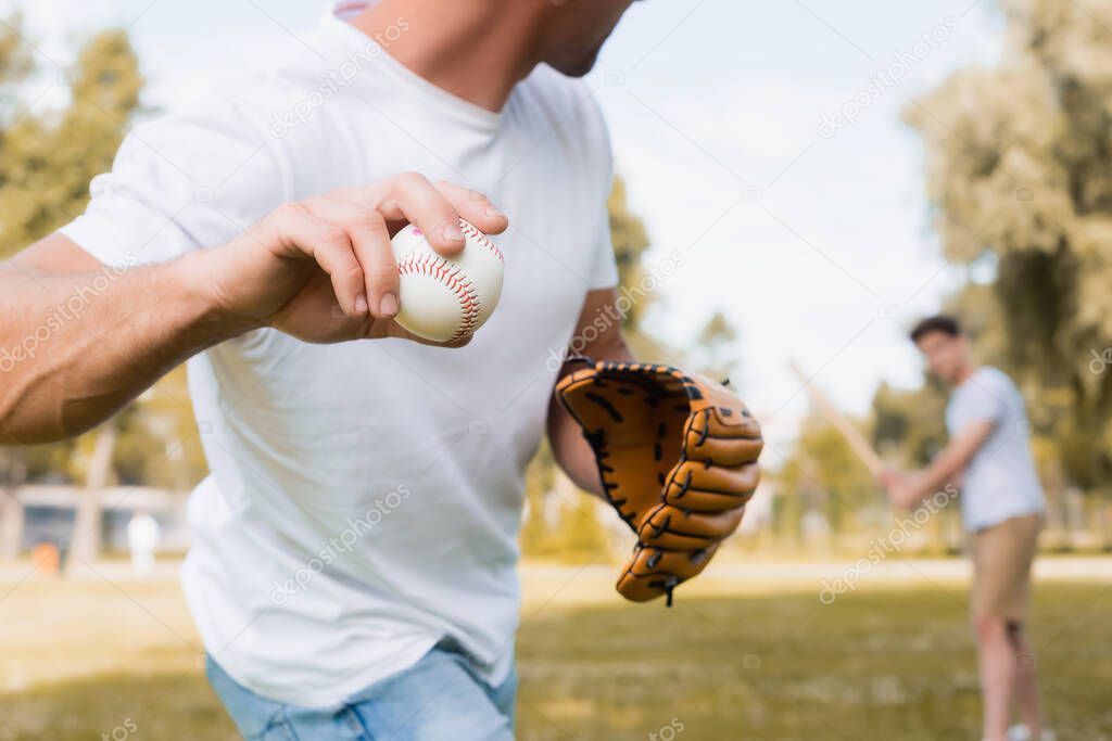 cropped view of man in leather glove playing baseball with teenager son in park 