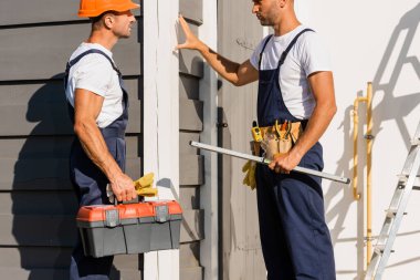 Alet edevat ve alet çantalı yapıcılar binanın ön cephesinde duruyorlar 