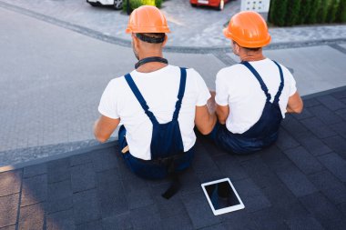 Binanın çatısında dijital tabletin yanında oturan inşaatçıların arka planı 