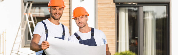 Horizontal crop of builders in hardhats holding blueprint outdoors 