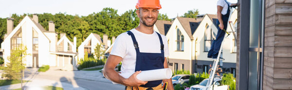 Horizontal concept of builder holding blueprint while working with colleague on roof of building 