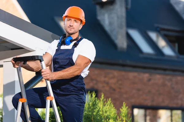 Bauarbeiter Arbeitskleidung Und Ohrenschützer Blicken Auf Kamera Auf Leiter Nahe — Stockfoto