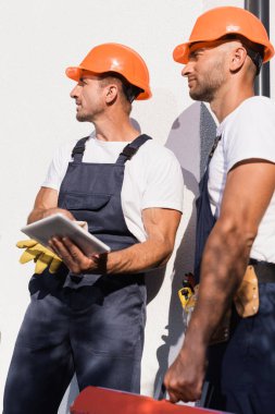 Dijital tabletli ve alet çantalı işçilerin seçici odak noktası binanın ön cephesinde duruyor 