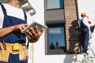 Meslektaşı evin ön cephesinde merdivende dikilirken, el işçisinin dijital tablet kullanarak seçici odak noktası 