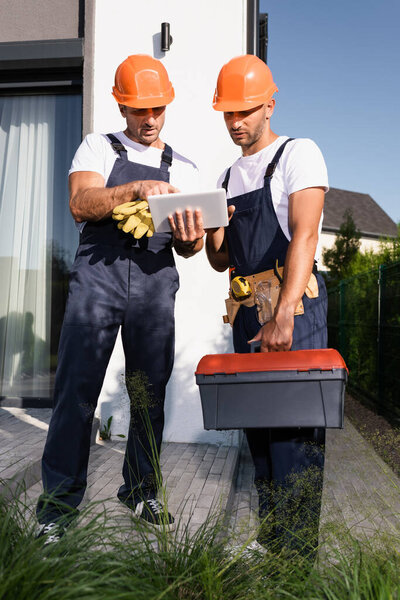 Selective focus of builders with tool belt and toolbox using digital tablet on urban street 