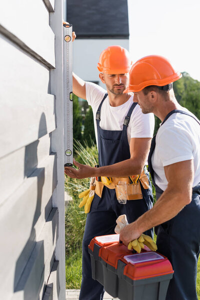 Selective focus of workmen with tools using spirit level while working with facade of building 