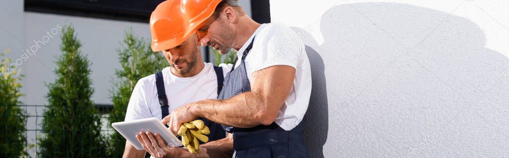 Panoramic orientation of handymen in workwear using digital tablet near house 