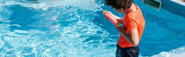 Havuz başında su tabancasıyla oynayan panoramik bir çocuk.