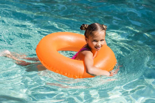 child looking at camera while floating in pool on swim ring