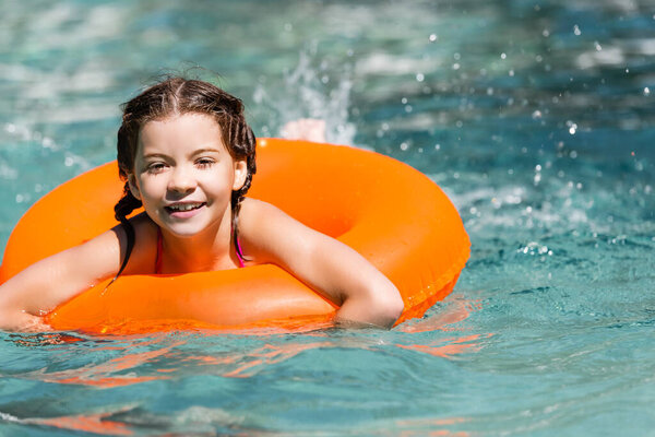 pleased girl swimming in pool on inflatable ring near water splashes