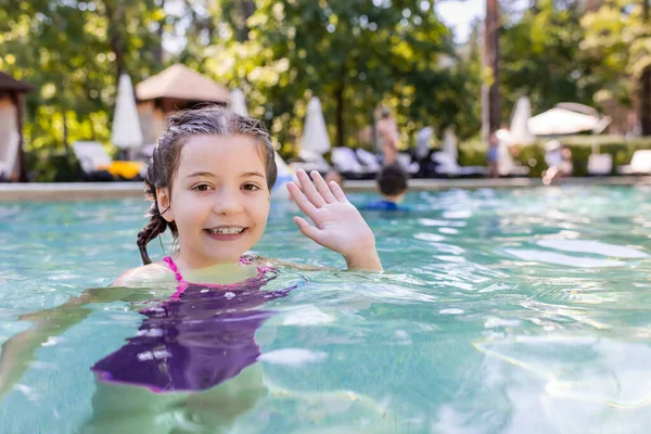 Vrolijk Meisje Zwembad Kijken Naar Camera Zwaaien Hand — Stockfoto