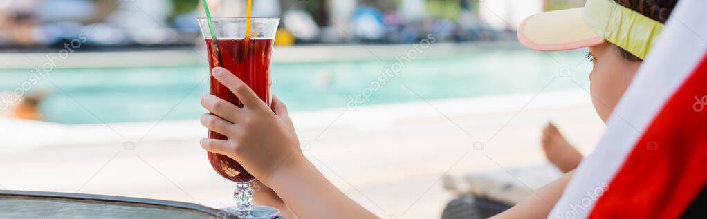 horizontal image of girl in sun visor cap holding cocktail glass while resting in deck chair