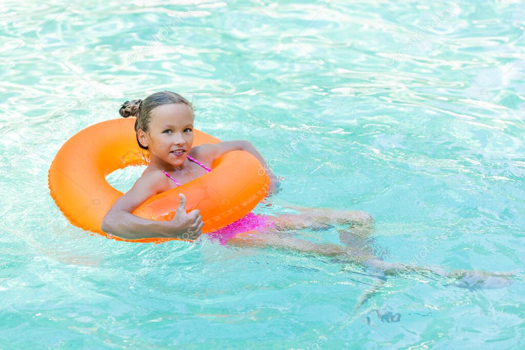 pleased girl floating in pool on inflatable ring and showing thumb up