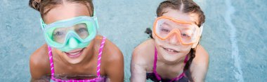 overhead view of two girls in swim masks looking at camera near poolside, horizontal crop clipart