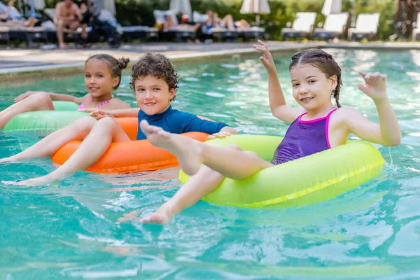 Amigos Alegres Mirando Cámara Mientras Flotan Piscina Anillos Natación Multicolores — Foto de Stock