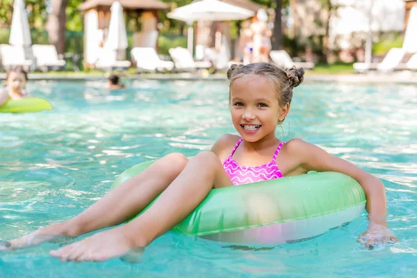 child looking at camera while floating in pool on inflatable ring