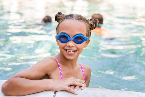 girl in swim goggles looking at camera at poolside 