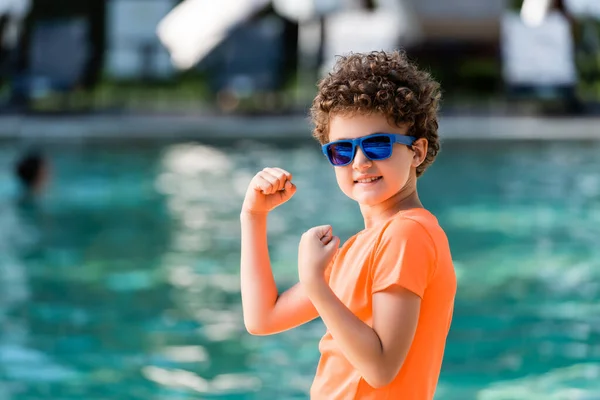 Curly Boy Orange Shirt Sunglasses Demonstrating Strength While Looking Camera — Stock Photo, Image