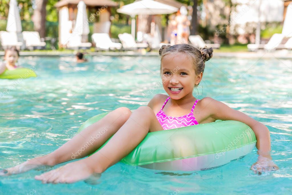 child looking at camera while floating in pool on inflatable ring