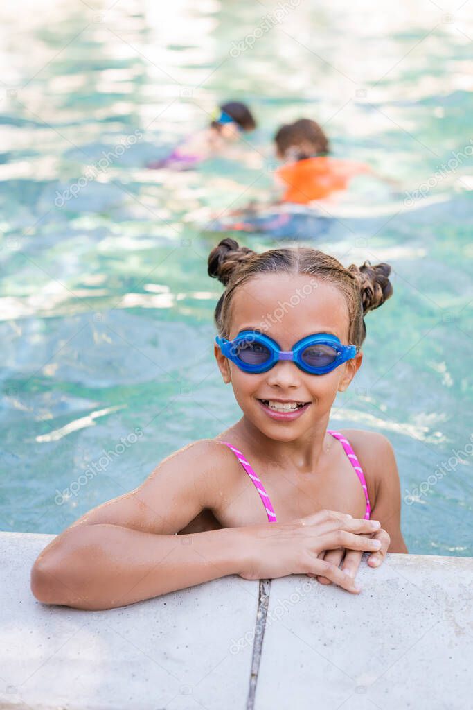 child in swim goggles looking at camera at poolside
