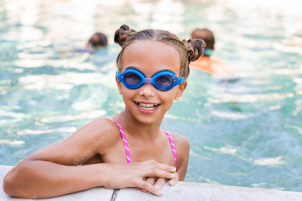 girl in swim goggles looking at camera at poolside 