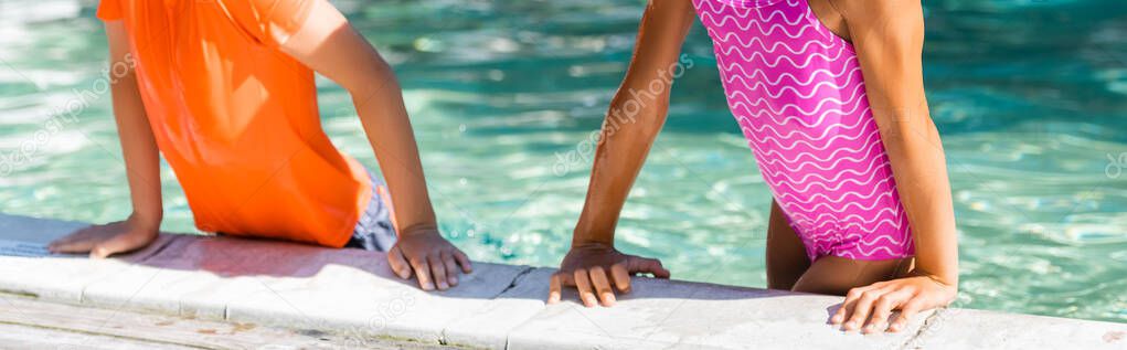cropped view of girl in swimsuit and boy in t-shirt leaning on poolside, panoramic shot