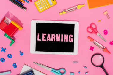 Okul kırtasiyesinin yakınındaki ekranda pembe harfleri öğrenen dijital tabletin üst görünümü 