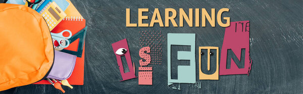 horizontal image of backpack with multicolored school supplies on black chalkboard with learning is fun lettering, top view