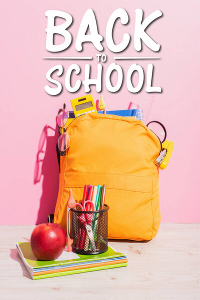 packed school backpack near notebooks, pen holder with felt pens and scissors, ripe apple and beck to school lettering on pink