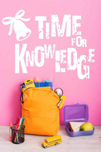 yellow backpack with school supplies, lunch box, toy school bus and pen holder with felt pens near time for knowledge lettering on pink