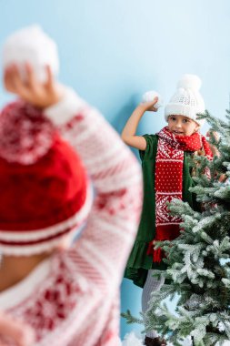 Mavi şapkalı ve eşarplı kızın elinde kartopu tutarken kardeşiyle oynadığı seçici odak noktası. 