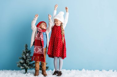 Çocuklar kışın giyinmiş, elleri yukarıda, ayakta birbirlerine mavi gözlerle bakıyorlar.