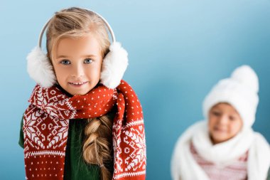 Kışın kulaklıklı kızın seçici odak noktası mavi elbiseli oğlanın yanındaki kameraya bakması.