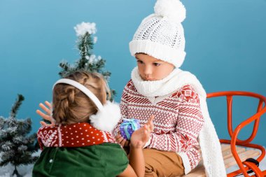 Örgü şapkalı oğlanın seçilmiş odak noktası. Hediye tutarken hünerli bir şekilde oturuyor ve kışın mavi kulaklık takan kıza bakıyor.